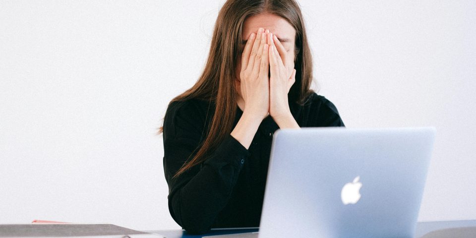 Woman feeling stressed and overwhelmed at her desk while working remotely on a laptop.