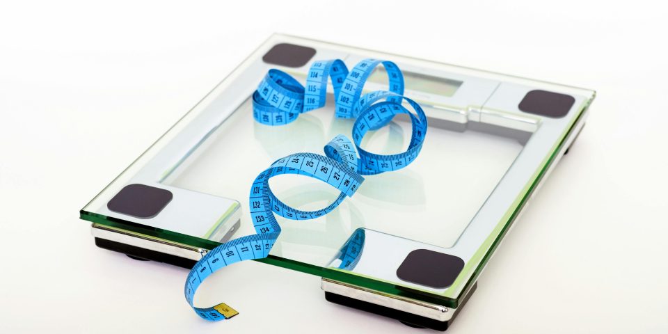 A digital glass weighing scale with a blue measuring tape, symbolizing weight management.